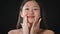 Seasonal skin moisturizing. Young beautiful asian woman applying nourishing cream on her cheeks, smiling to camera