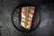 Seasoned fresh pork ribs with spices on a round black plate on a black background