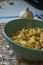 Seasoned rigatoni pasta in a green bowl on a burlap mesh with a garlic bulb in the background