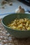 Seasoned rigatoni pasta in a green bowl on a burlap mesh with a garlic bulb in the background