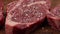 Seasoning raw ribeye beef steaks with pepper
