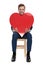 Seated fashion man holds a big red heart in hands