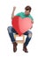 Seated happy man celebrates victory with red heart in hands