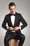 Seated man in tuxedo buttoning his coat and looks away