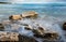 Seawaves splashing onto the sandy coast with pebbles and blue cloudy sky.