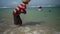 Seaweed farmer walks through waves on Indonesian beach harvesting loose seaweed