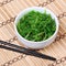 Seaweed with sesame seeds with chopsticks in ceramic bowl on bamboo mat. Chuka salad.