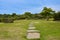 Secluded area with rocky steps, grass, and trees with blue sky in Camellia Hill of Jeju Island, South Korea.