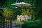 Secluded table with chairs and comfortable rattan chairs under a sunshade among green vegetation for a lovely dinner in the summer