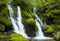 A secluded waterfall surrounded by a lush fern-covered gorge, the water cascading into a clear pool below