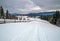 Secondary countryside alpine road in remote mountain village, snow drifts and wood fence on wayside