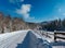 Secondary countryside alpine road to remote mountain hamlet through snowy fir forest, snow drifts and wood fence on wayside