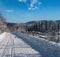 Secondary countryside alpine road to remote mountain hamlet through snowy fir forest, snow drifts and wood fence on wayside