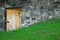 Secret Door to Hidden Room in Old Stone Wall on Grassy Slope