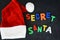 Secret Santa text with colorful magnetic letters on blackboard near Santaâ€™s red hat