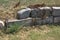 Section of decorative rough-hewn drystone blocks stacked on one another to create a retaining wall with grass growing through the