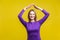 Secured life, insurance concept. Portrait of cheerful woman showing home roof gesture. isolated on yellow background