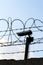 Security camera behind barbed wire fence on the wall, prison, security, crime or illegal immigration concept, blue sky