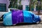 Sedan car at outdoor parking area covered by blue and purple fabric car cover
