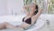 Seductive girl in bikini rests in large bathtub at home