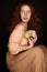 Seductive redhead woman in beige clothes holding fresh green apple