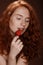 Seductive redhead woman eating red strawberry, on brown