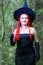 Seductive sorceress with red hair in a pointed hat in the forest is engaged in magic with a candle.