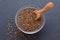 Seeds of cumin, caraway in a bowl and wooden scoop on black background