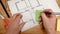 Seen from above, the hand of an interior designer sticks a green post it on a technical drawing of a new house, ideal