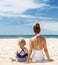 Seen from behind mother and child in swimsuits sitting at beach