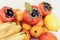 A selection of arranged different fresh fruits of bananas, mandarins, persimmons and lemons on white background close up