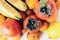 A selection of arranged different fresh fruits of bananas, mandarins, persimmons and lemons on white background close up