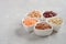 Selection of dry legumes, lentils and peas in white bowls on gray concrete background.