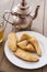 A selection of Moroccan pastries on a plate. To the left a glass of mint tea and in the back a traditional tea pot