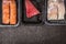 Selection of raw colorful fish fillets : salmon, tuna and codfish in plastic boxes on dark rustic background, top view, border, pl