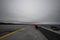 Selective color shot of a person with a red umbrella walking on the along the shore on a rainy day