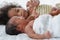 Selective focus of African newborn baby boy crying lying on white bed and little older sister trying to comforting by holding hand