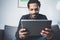 Selective focus.Attractive bearded African man using tablet while sitting on sofa in his modern office.Concept of young