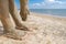 Selective focus on beautiful female foot with bright red pedicure on the beach sand. Hands smear healing mud on the