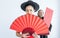 Selective focus beautiful happy Asian rich woman wearing red qipao or dress, smiling, holding folding fan with blur male bodyguard