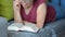 Selective focus on book read by caucasian woman with short haircut in burgundy T-shirt and jeans lying on gray sofa with pillows.