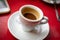 Selective focus closeup shot of a white cup of freshly made espresso placed on the red table