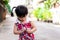 Selective focus. Cute Asian girl tries to button up her red checkered shirt. Children learn to wear clothes. Child are walking on