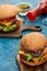 Selective focus of delicious cheeseburger on wooden board on blue textured surface