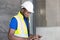 Selective focus at face of Black African foreman at building construction site, wearing protective hat and safety equipment while