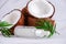 selective focus glass bottle with coconut oil on a blurred background of cracked coconuts and palm leaves