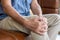 Selective focus at hand of old senior Asian man sitting at sofa touching knee and suffer from the pain and injury. Healthcare and