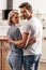 Selective focus of handsome boyfriend and attractive girlfriend hugging and standing in kitchen while looking