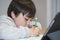 Selective focus kid using green pe colouring, Candid shot child painting on white paper with burrly tablet foreground, Young boy