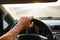 Selective focus man`s hand on steering wheel, driving a car at sunset. Travel background